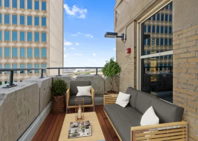 Rooftop patio with modern seating, a small table, and a city view. Urban buildings and a plant add to the decor at Merchants Plaza.