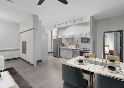 Modern open-concept kitchen and living area with a dining table set for four, light gray cabinetry, and stainless steel appliances at Merchants Plaza.