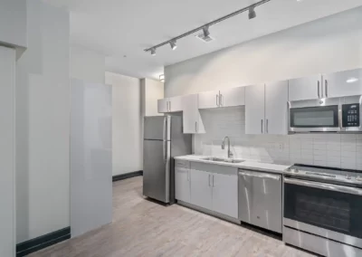 Modern kitchen with stainless steel appliances, white cabinetry, and grey countertops, featuring a track lighting system at Merchants Plaza.
