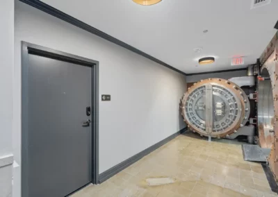 A hallway with a gray door on the left and a large circular vault door on the right at Merchants Plaza.