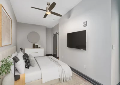 Modern bedroom with a bed, wall-mounted TV, ceiling fan, stylish decor, and a door leading to an adjoining room at Merchants Plaza.