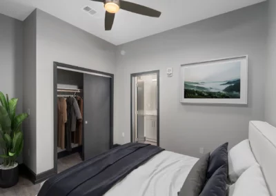 Modern bedroom with neutral tones, a bed, potted plant, closet with clothing, and a framed landscape picture on the wall at Merchants Plaza.