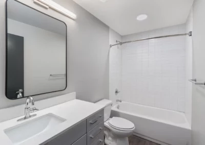 Modern bathroom with a large mirror, sink, toilet, and a bathtub with a white tiled wall at Merchants Plaza.