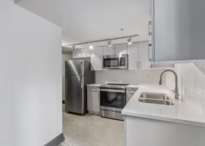Modern kitchen with stainless steel appliances, white cabinets, double sink, and track lighting at Merchants Plaza.