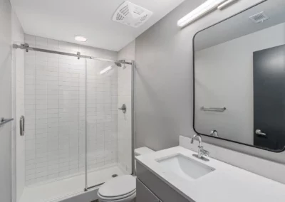 Modern bathroom with glass shower, white tiles, large mirror, sink with faucet, and minimalistic decor at Merchants Plaza.