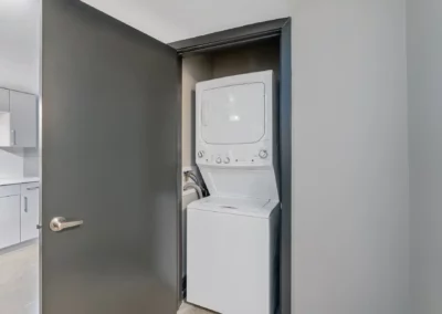 A small laundry area with a stacked washer and dryer unit behind an open gray door in a modern apartment at Merchants Plaza.
